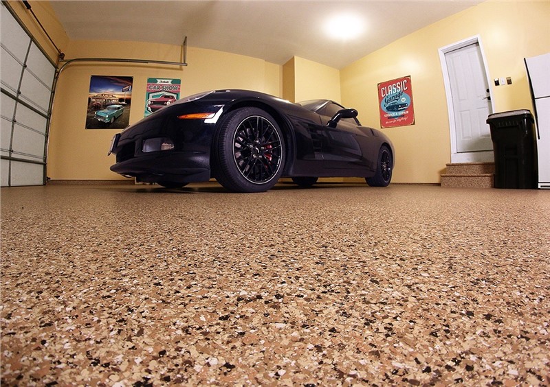 A black sports car in a garage with a floor that looks like brown granite with lots of flecks.