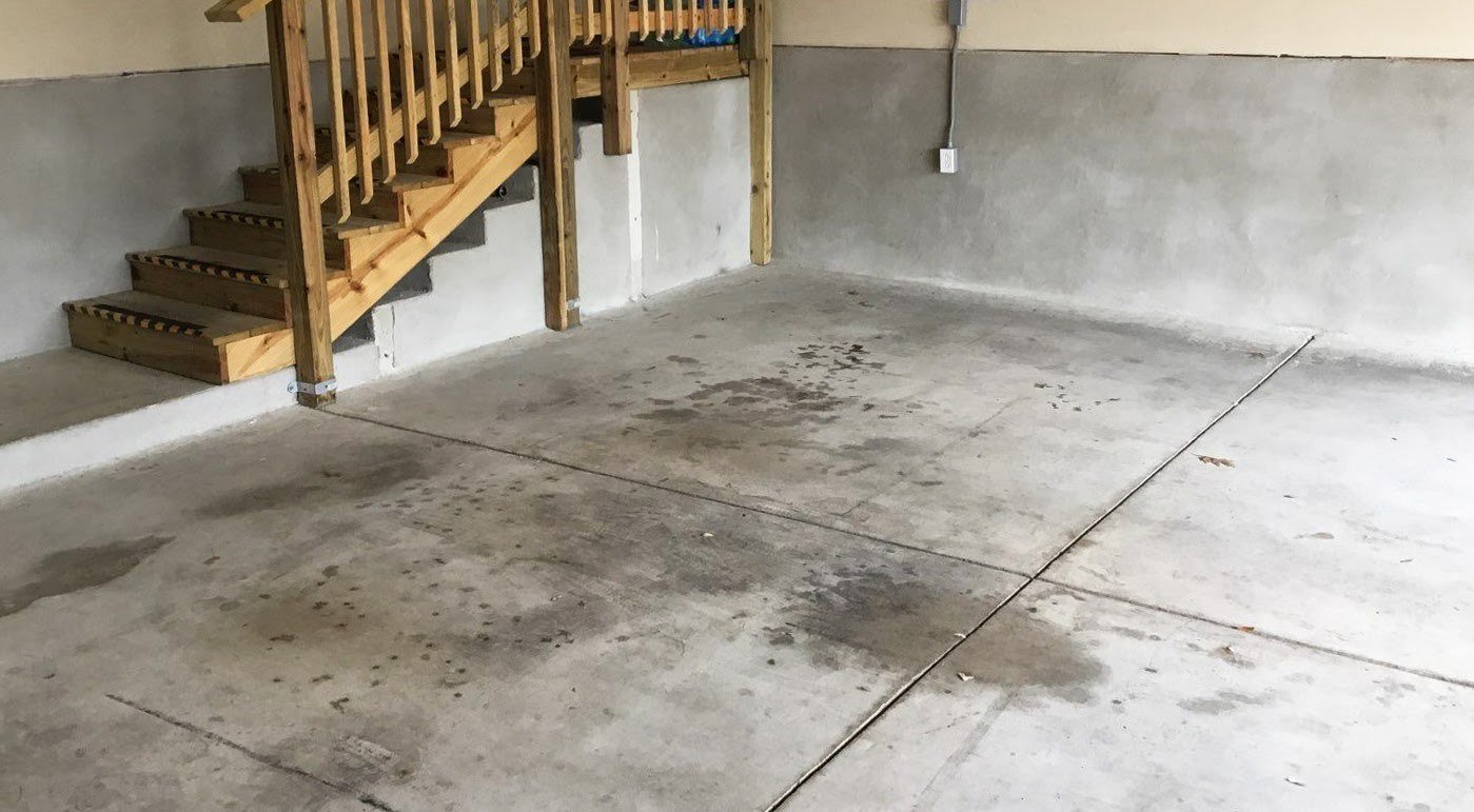 The inside of an empty garage with concrete going halfway up the walls and a wooden staircase leading to a door in the left corner.
