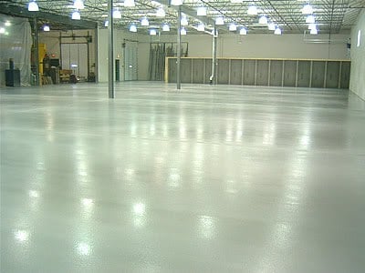The inside of a large building that looks like a warehouse with fluorescent lights and a grey floor.