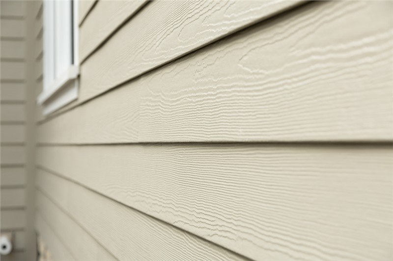 A close shot of the side of a home at an angle. The horizontal lap siding is a beige color with a cedar finish. 