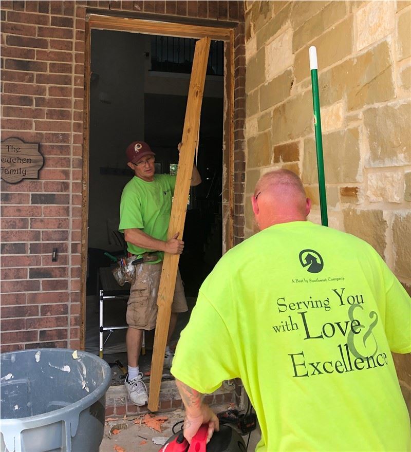 Two men in bright neon yellow shirts in an open doorway replacing the door system. One man is walkin…