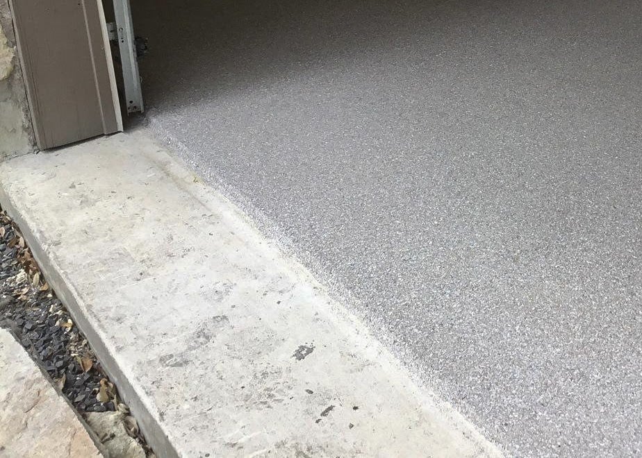 A close up of a garage floor near the garage door opening with a grey colored coating that stops right before the door.