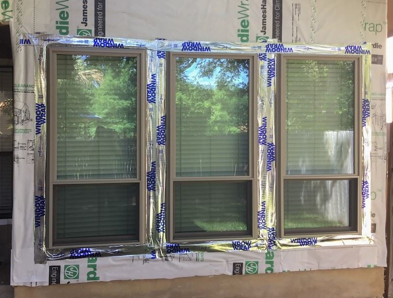 Flashing tape The side of a house with three windows, the walls are exposed under construction and a silver tape i…