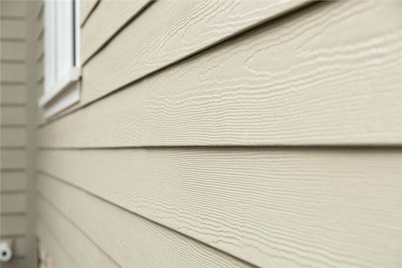 A close shot of the side of a home at an angle. The horizontal lap siding is a beige color with a ce…
