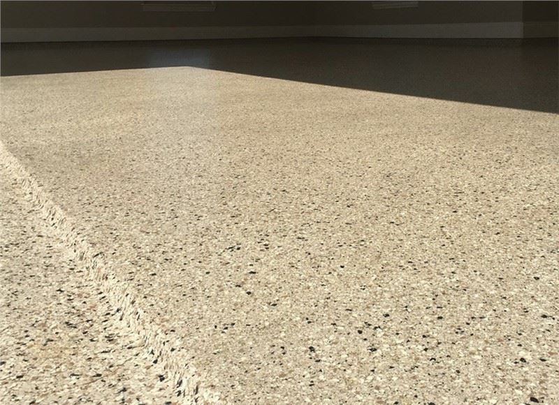A close up of a garage floor apron and lip with a concrete coating that looks like granite with tan, white, and black vinyl chips in the coating.