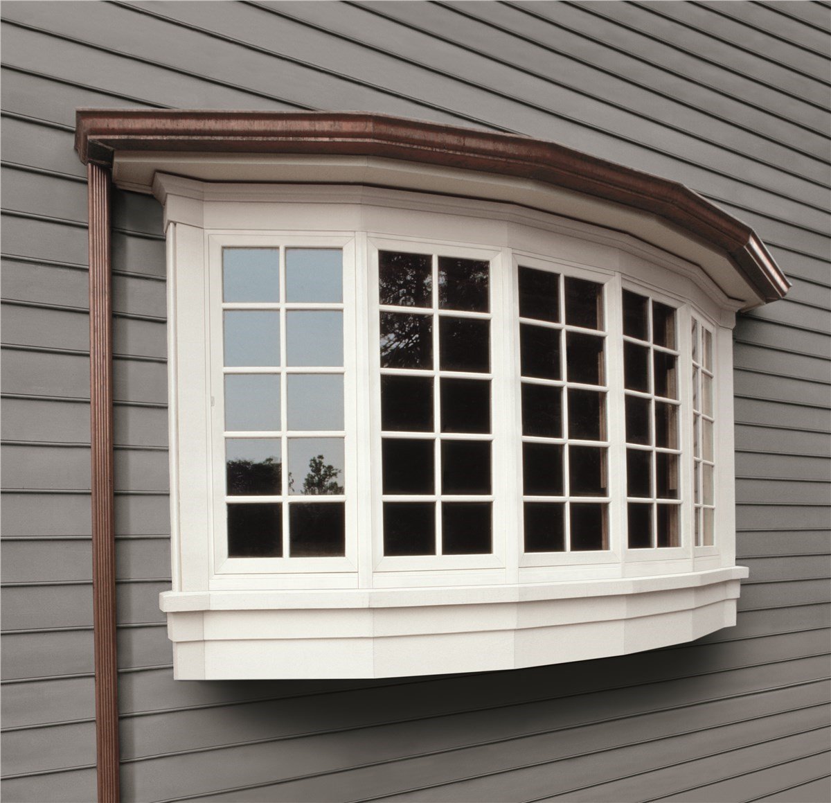 A bay window with a white frame and many panes of glass sits on a gray-sided wall.