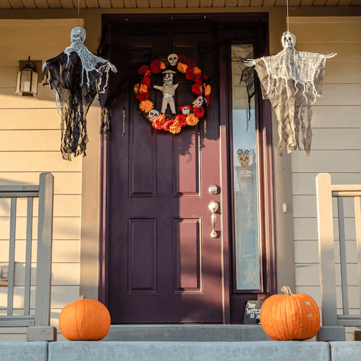 The front entryway of a home with pumpkins, hanging ghosts, and a voodoo doll wreath on the road.